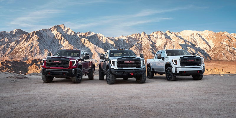 Three GMC sierras parked side by side with mountains behind